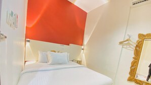 Ein Hotelzimmer mit einem Bett, weißer Bettwäsche, einer roten Akzentwand, einem goldfarbenen Spiegel und einem kleinen Nachttisch.