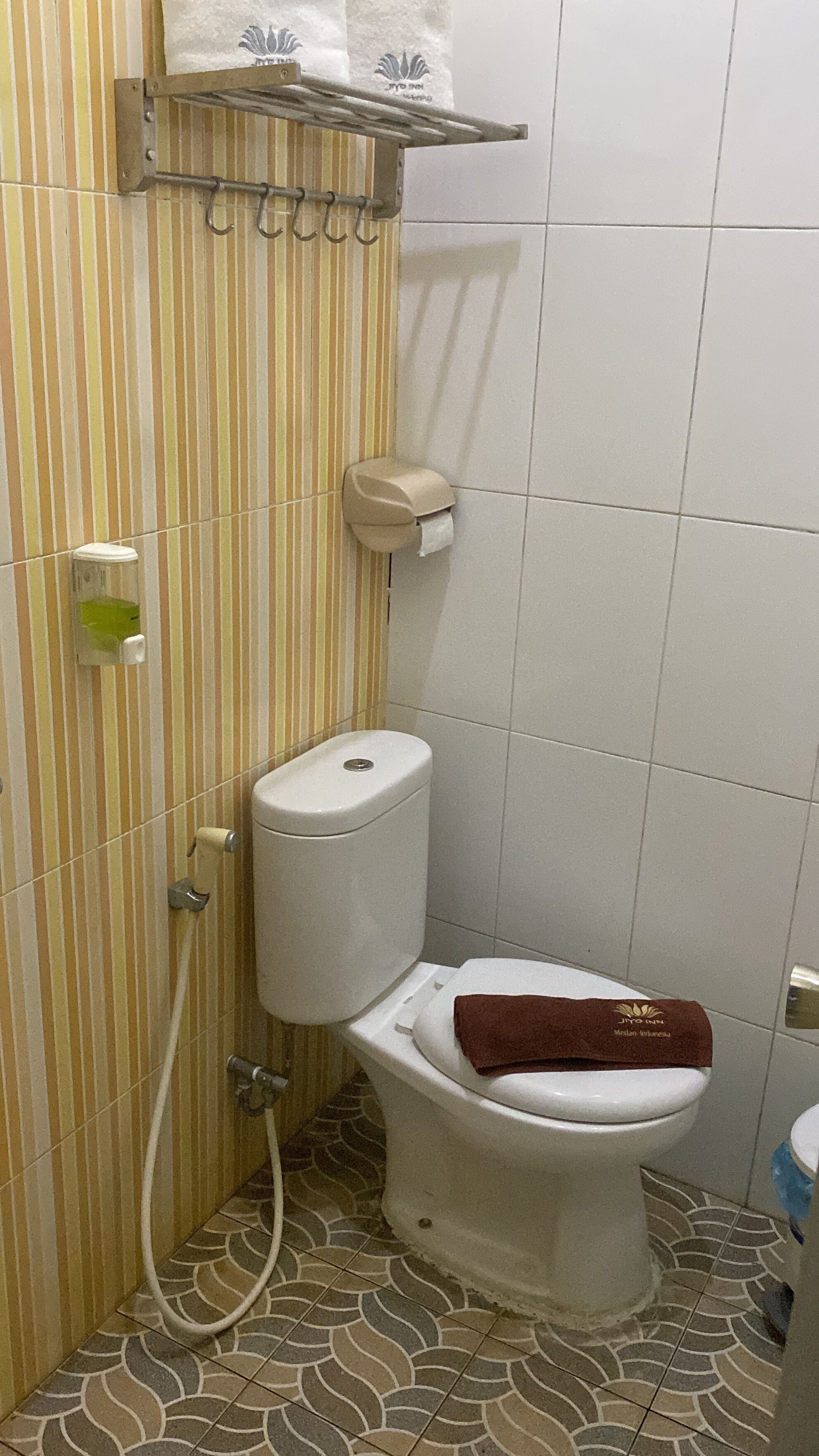 Une salle de bain avec un mur à rayures, des toilettes sur lesquelles est posée une serviette marron, un distributeur d’essuie-tout et un distributeur de savon.