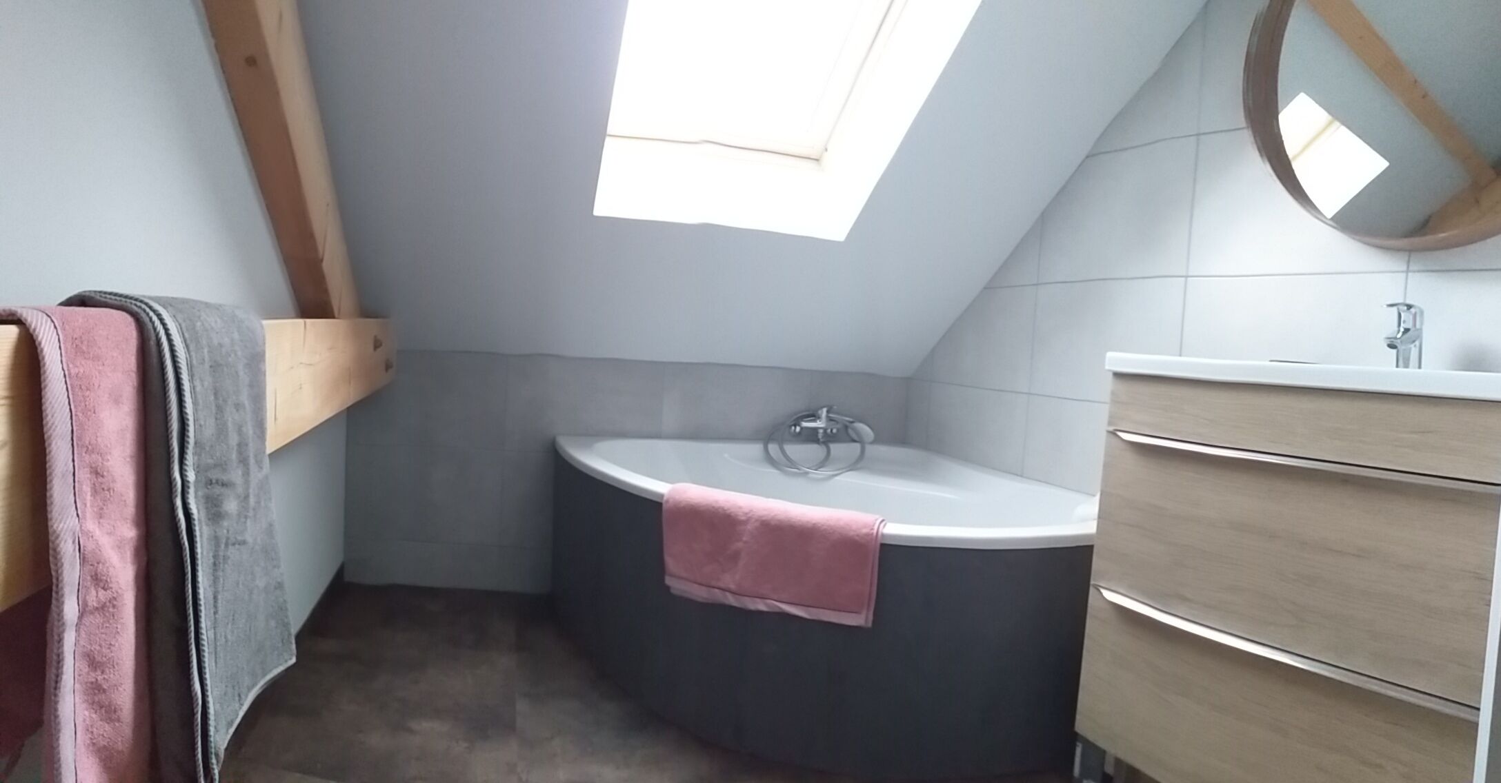 A small bathroom with a skylight, a bathtub, and a wooden vanity.
