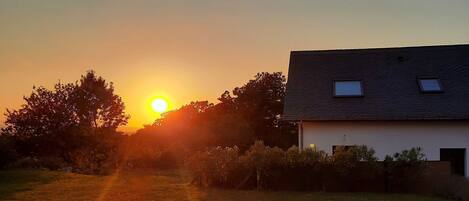 Un atardecer sobre un campo cubierto de hierba, con una casa al fondo.