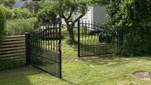 A residential property with a gated entrance, a wooden fence, and a well-maintained lawn.