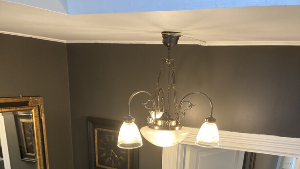 A staircase with a white railing leading to a room with a chandelier and a framed clock on the wall.