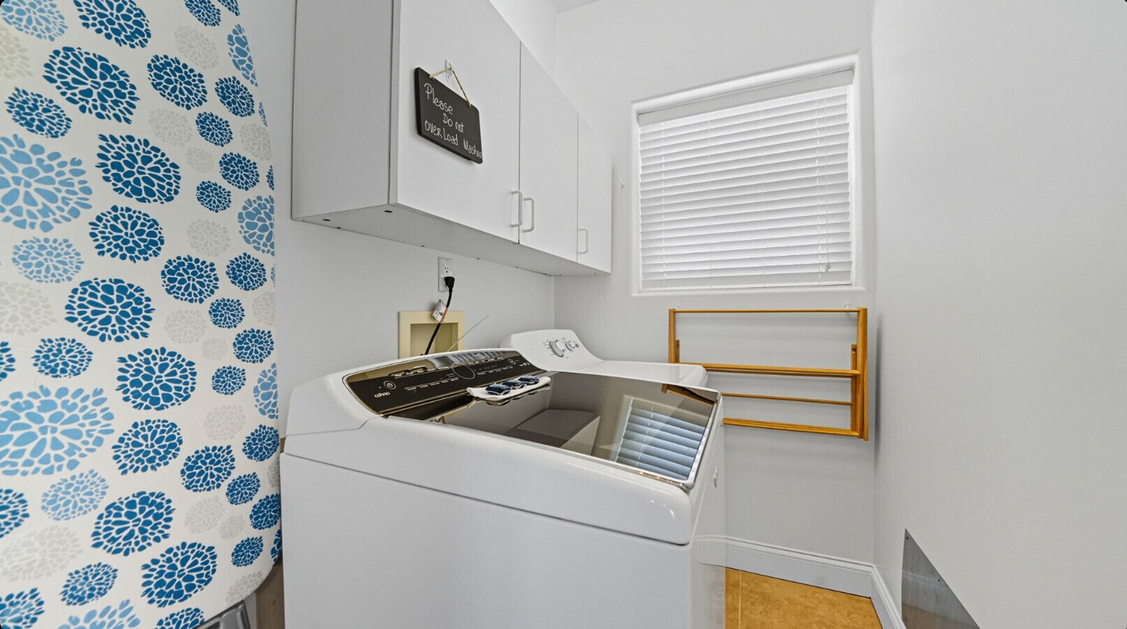 Une cuisine compacte équipée d’un lave-linge et d’un sèche-linge intégrés, d’un petit placard et d’une fenêtre avec des stores.