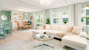 A living room with a white sofa, a glass coffee table, a dining area with a table and chairs, and a chandelier.