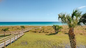 A wooden boardwalk leading to a beach with palm trees and a clear blue sky.