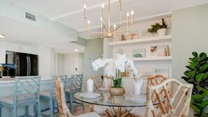 A dining area with a glass table surrounded by wicker chairs and a chandelier.