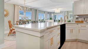 A modern kitchen with a large island, white cabinetry, and gold handles.