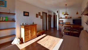 Un salon avec des meubles en bois, un canapé, une table à manger et, au fond, un coin cuisine.