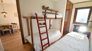 Une chambre avec un lit superposé, une échelle en bois, un bureau avec des chaises et une fenêtre donnant sur un beau paysage.