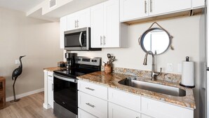 Une cuisine moderne avec des armoires blanches, un comptoir en granit, un évier en acier inoxydable, un four à micro-ondes, un four traditionnel et un miroir décoratif.