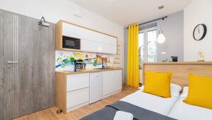 Et moderne hotelværelse med et træskab, et tekøkken, en seng med gule puder og et stort vindue med gardiner.