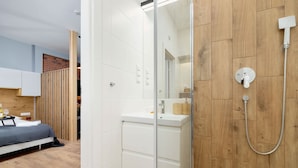 A modern bathroom with a wooden vanity, a glass shower enclosure, and a white sink. - Comfortable Studio | Workspace | Close to the Marketplace (Kraków)