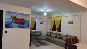 Un salon avec un canapé, une table basse et une table à manger. Un tableau représentant un bateau est accroché au mur.