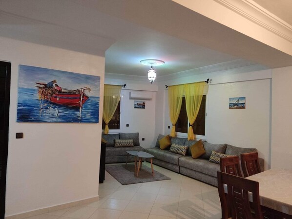 A living room with a sofa, a coffee table, and a dining table. There is a painting of a boat on the wall.
