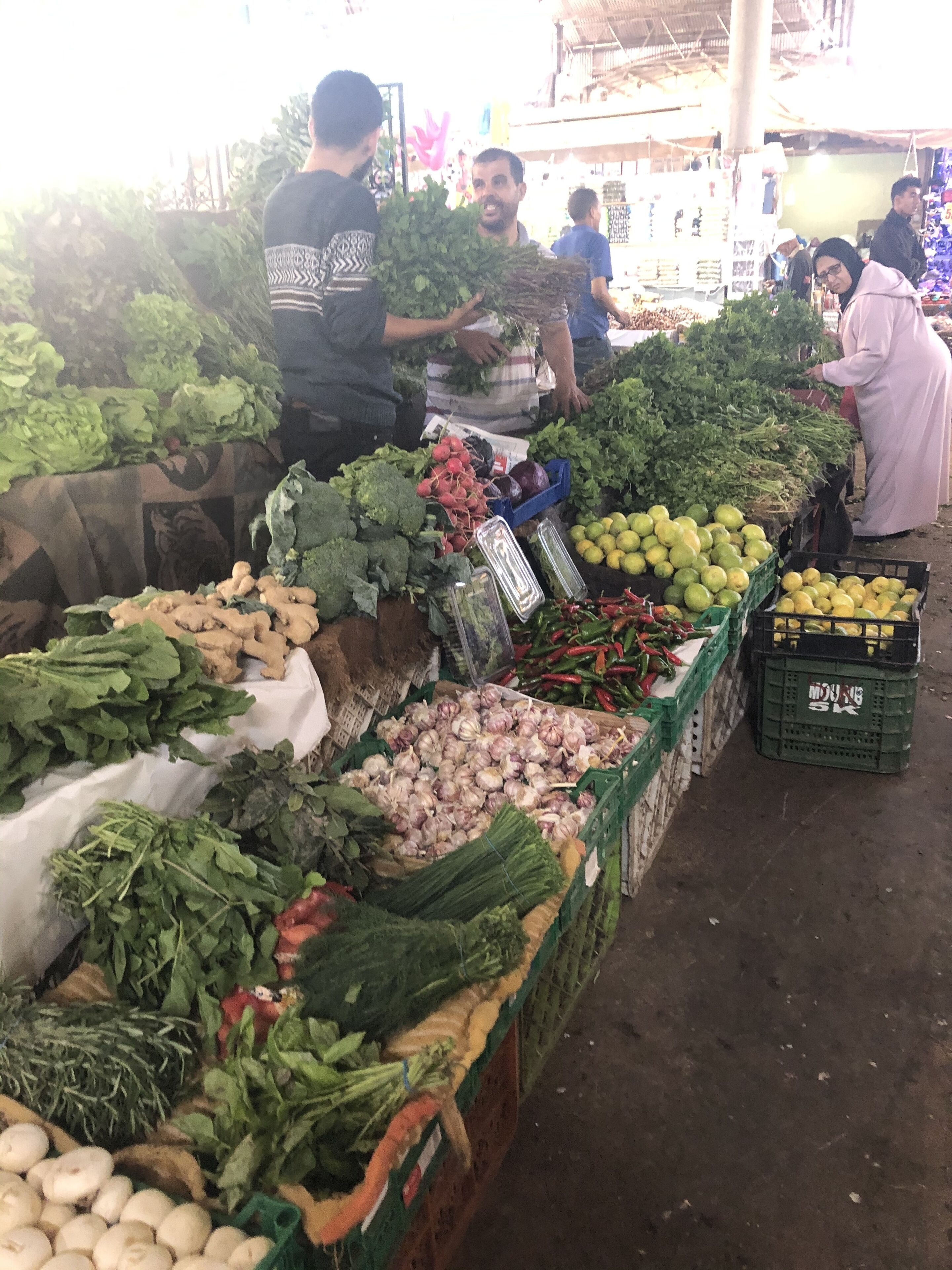 A market stall with various vegetables and fruits, including leafy greens, radishes, and citrus fruits.