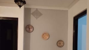 Un couloir avec deux chaises en bois dotées de coussins à motifs, une horloge murale et une lanterne décorative.