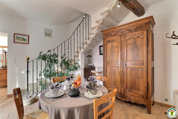 A dining area with a round table set for four, a staircase with a metal railing, and a wooden cabinet.