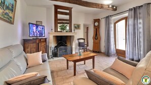 Uma sala de estar com lareira, vigas de madeira, televisão e um relógio.