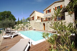 A stone building with a swimming pool, lounge chairs, and potted plants.