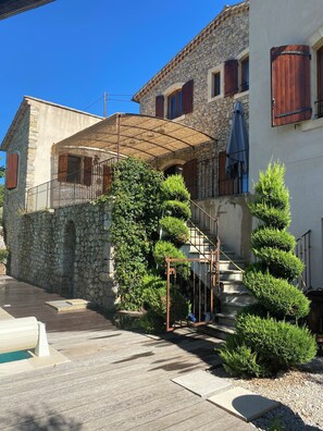 A stone building with a wooden staircase, a covered outdoor area, and a pool.
