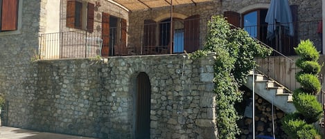Edificio de piedra con piscina, un porche cubierto y una escalera que lleva a un balcón.