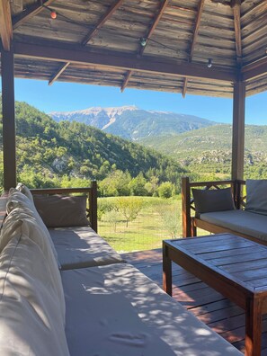 A wooden deck with a sofa and table, overlooking a mountainous landscape.
