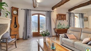 Uma sala de estar acolhedora com um sofá de madeira, uma mesa de centro de madeira, uma cadeira de madeira, um relógio e vista através de uma porta de vidro.