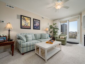 A living room with a striped sofa, a white coffee table, a green armchair, and a large window with a city view. - Beautiful 3 Bedroom, 3 Bath Oceanblock Condo Mid-Town with Indoor Pool (Ocean City)