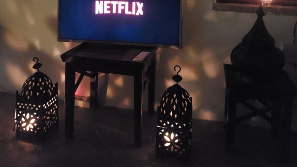 A television displaying the Netflix logo, a mirror, and two decorative lanterns in a dimly lit room. - Casa Balcón- Increíbles Vistas! (Saleres)