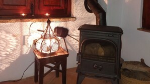 A cozy room with a wood-burning stove, a small table with a lamp, and a window with wooden shutters. - Casa Balcón- Increíbles Vistas! (Saleres)