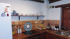 A kitchen with wooden cabinets, a built-in oven, a sink, and a shelf with glassware and a decorative plate. - Casa Balcón- Increíbles Vistas! (Saleres)