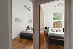 A bedroom with two beds, wooden flooring, a window with a view, and a door leading to another room.
