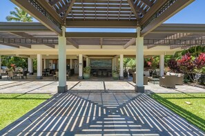 An outdoor covered patio area with seating arrangements, a central table, and potted plants. - Enjoy Ocean Views from Mauna Lani Point A105 (Kamuela)