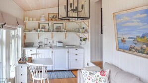 Une cuisine chaleureuse avec des meubles blancs, une table à manger entourée de chaises et un tableau représentant un paysage marin accroché au mur.