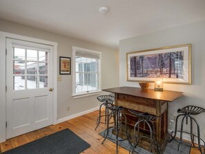 A room with a wooden table and four bar stools, a framed welcome sign, and a painting on the wall. - Bethel Village Carriage House Apartment (Bethel)