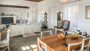 A spacious living room with a wooden dining table, white furniture, and a large window allowing natural light. - Gorgeous home in Sifnos (Sifnos)