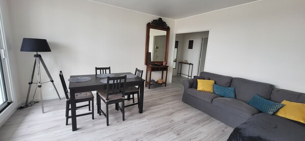Una sala de estar moderna con una mesa de comedor, sillas, un sofá con cojines, una lámpara de pie y un espejo.