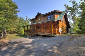 A log cabin with a porch, a covered staircase, and a gravel driveway.