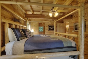 A wooden cabin bedroom with a bed, a ceiling fan, and a framed picture on the wall.