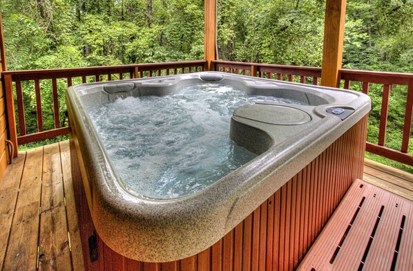A hot tub on a wooden deck with a forest backdrop.