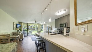 Une cuisine moderne dotée d’un grand îlot central, de tabourets de bar et d’un coin repas offrant une vue sur l’extérieur.
