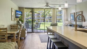 Une chambre d’hôtel avec un coin repas, un ventilateur de plafond et une vue sur un jardin aménagé et une piscine.