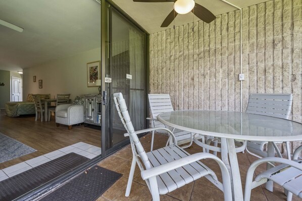 A dining area with a glass table and white chairs, a ceiling fan, and a textured wall. - Oceanfront Maui Sunset Condos ground floor in Kihei (Kihei)