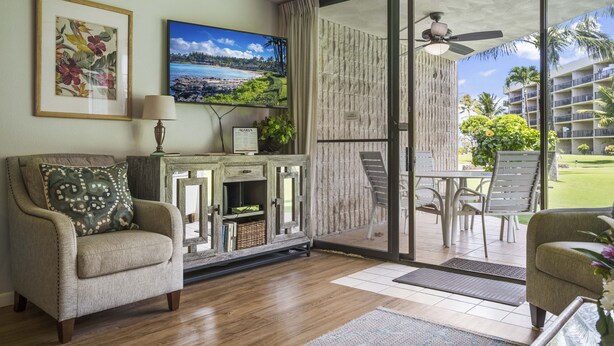 Un salon comprenant un canapé, un téléviseur et donnant sur un balcon aménagé avec du mobilier d’extérieur.