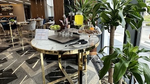 A hotel lobby with a round table displaying breakfast items, a sign indicating free charge, and large windows with a view of the street. - Trademark Collection By Wyndham Operla İstanbul Airport Hotels (Arnavutköy)