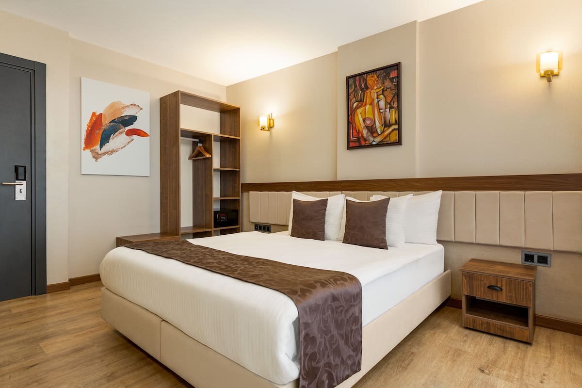 A hotel room with a large bed, a wooden nightstand, a wardrobe, and two wall-mounted light fixtures.