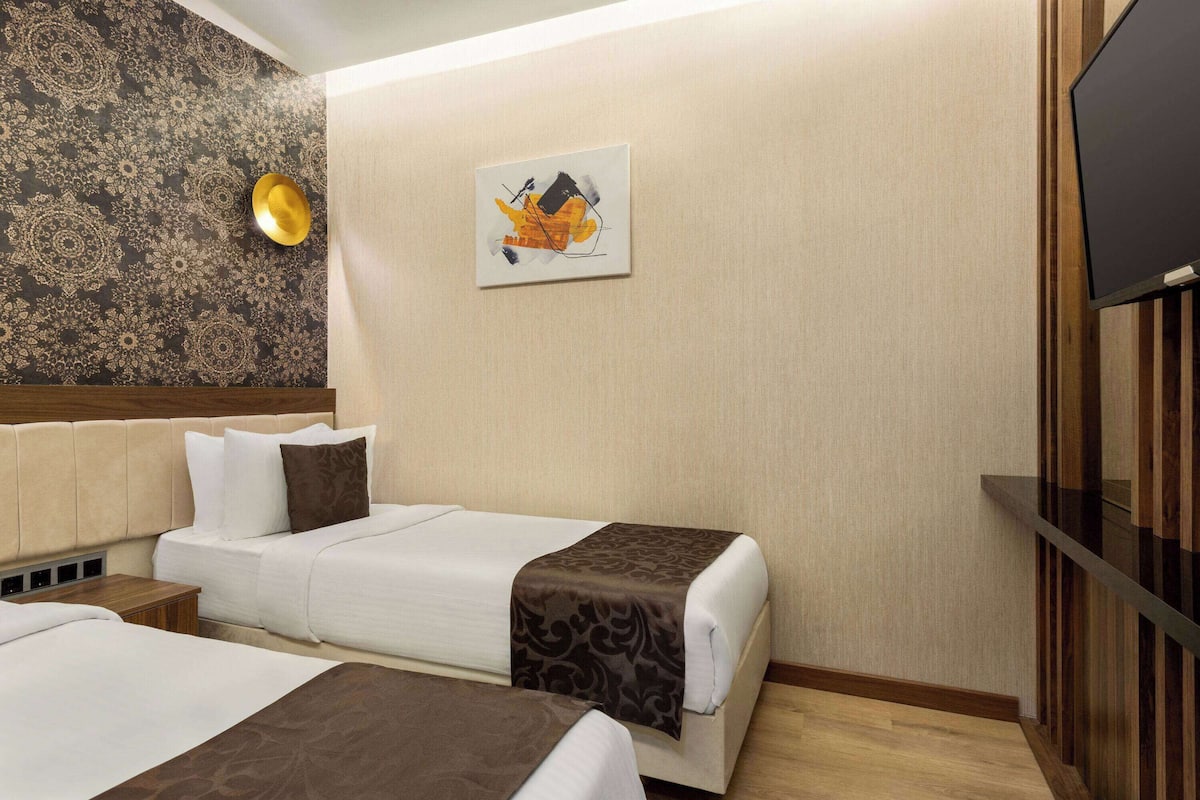 A hotel room with two beds, a large artwork on the wall, and a television on the right.