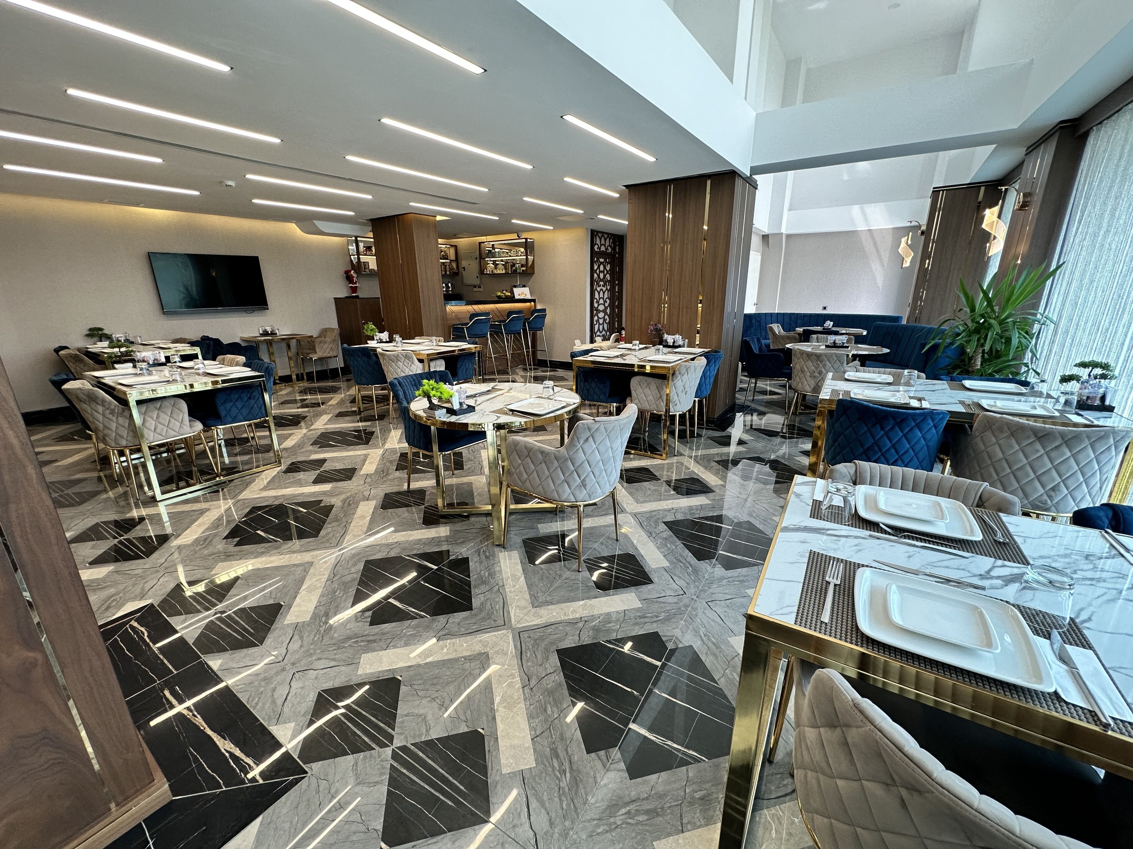 A modern restaurant with a geometric marble floor, contemporary furniture, and a central bar area.