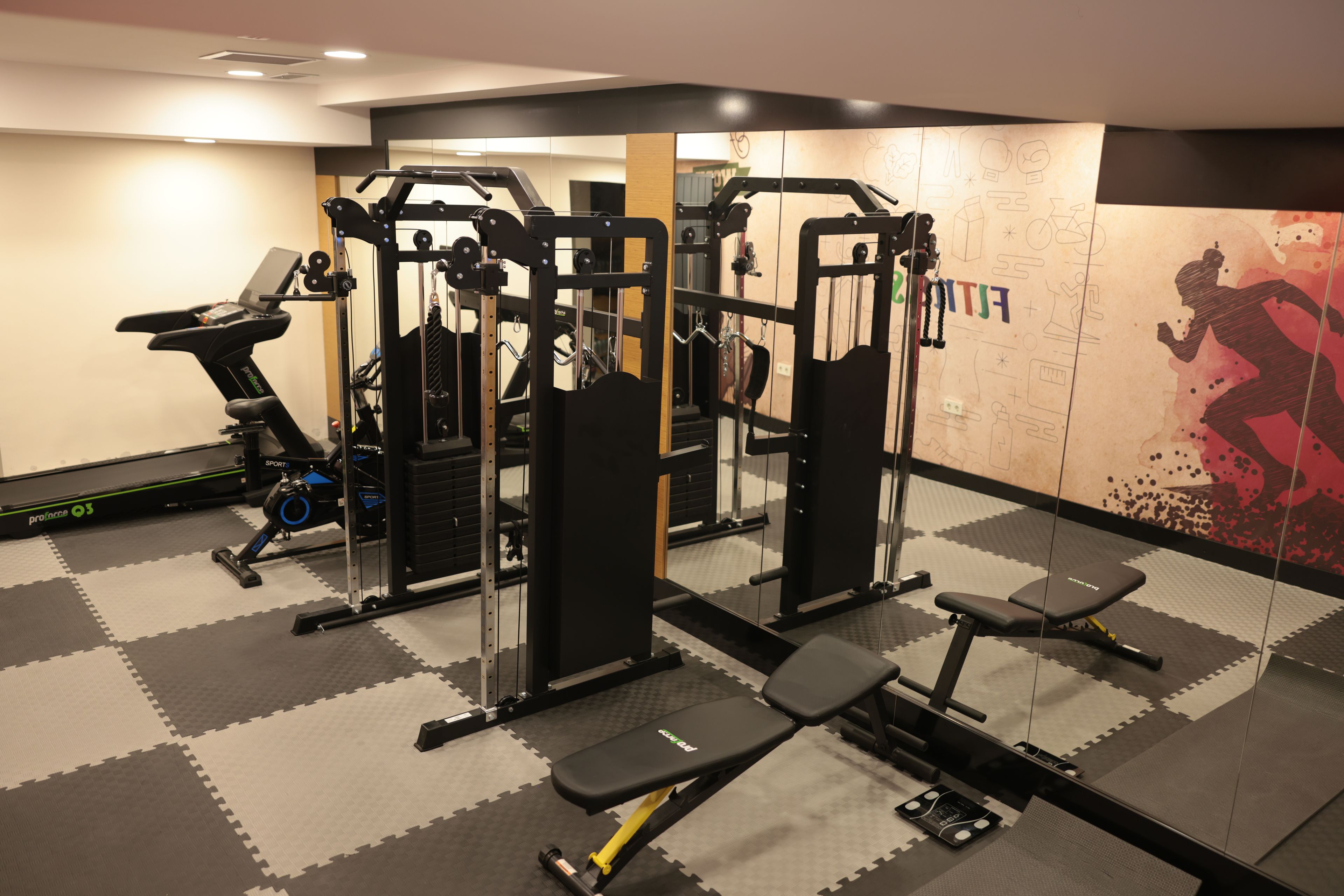 A gym with exercise equipment, a treadmill, and a wall with fitness-related graphics.