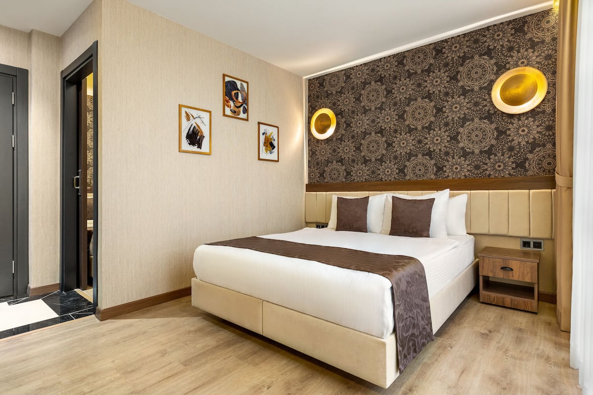 A modern hotel room with a large bed, a wooden nightstand, and a wall with patterned wallpaper and wall sconces.